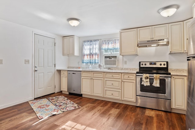 kitchen with appliances with stainless steel finishes, cream cabinetry, light stone counters, dark hardwood / wood-style flooring, and sink