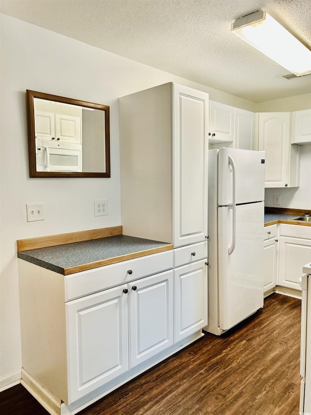 kitchen with dark wood-type flooring, white appliances, a textured ceiling, and white cabinets