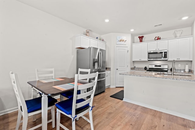 kitchen featuring sink, light stone counters, light wood-type flooring, stainless steel appliances, and white cabinets