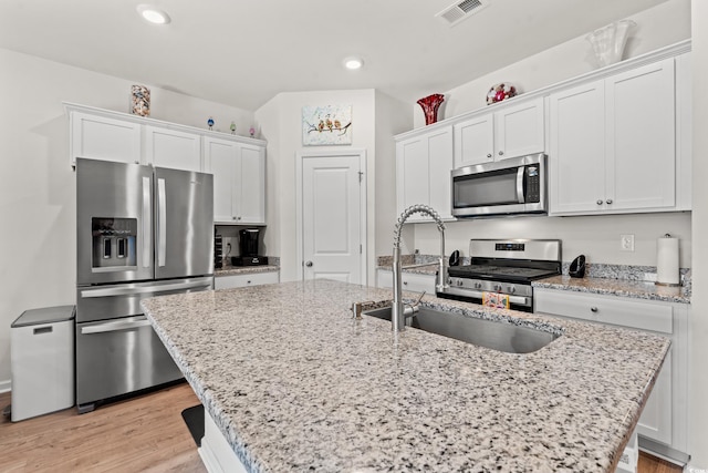 kitchen with an island with sink, appliances with stainless steel finishes, sink, and white cabinets