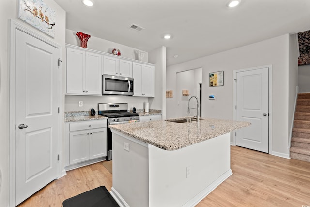 kitchen with sink, white cabinetry, a center island with sink, light hardwood / wood-style flooring, and appliances with stainless steel finishes