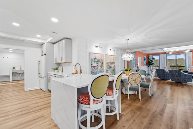 kitchen with visible vents, white cabinets, freestanding refrigerator, a sink, and a notable chandelier