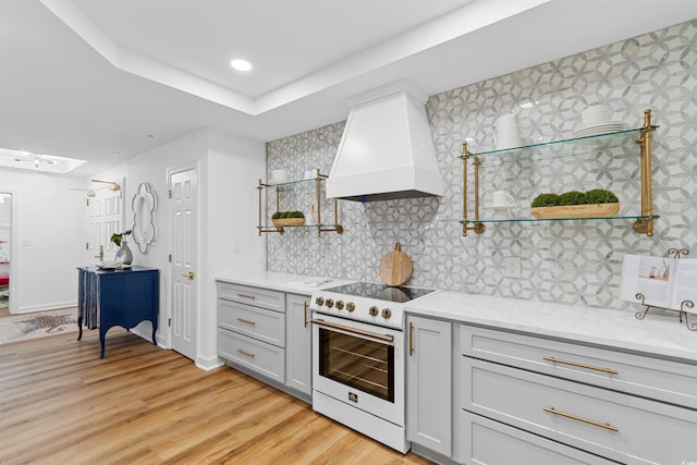 kitchen with light stone counters, light wood finished floors, custom exhaust hood, open shelves, and white electric range