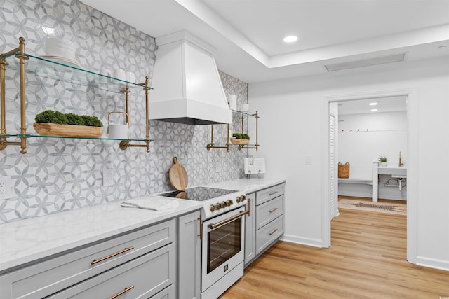 kitchen featuring light stone counters, premium range hood, light wood-style floors, tasteful backsplash, and white electric range oven