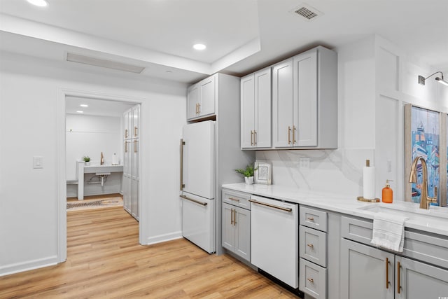 kitchen featuring white appliances, light wood finished floors, visible vents, light stone counters, and gray cabinetry