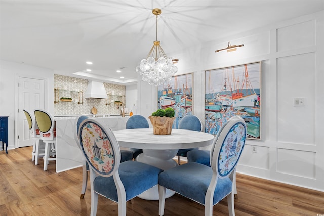 dining area with light wood-style floors, a decorative wall, an inviting chandelier, and recessed lighting