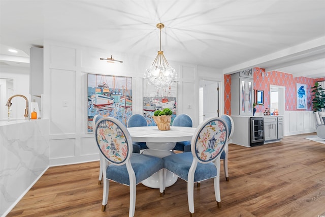 dining area with wine cooler, a decorative wall, a wainscoted wall, wood finished floors, and wallpapered walls