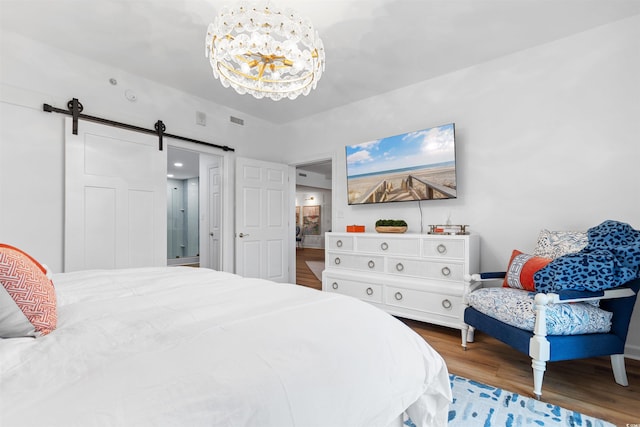 bedroom with a notable chandelier, a barn door, visible vents, and wood finished floors