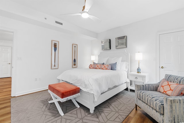 bedroom with a ceiling fan, visible vents, baseboards, and wood finished floors