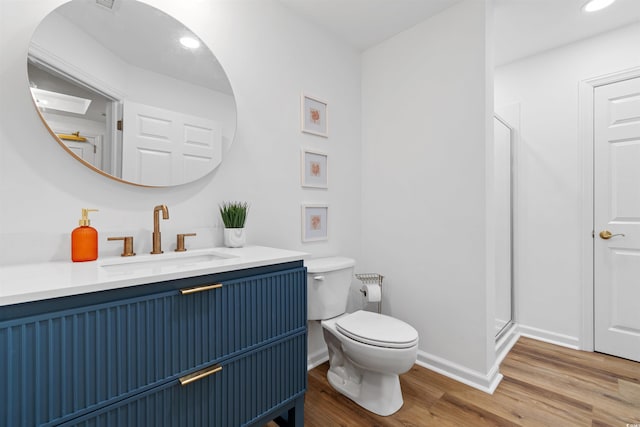 bathroom with toilet, a shower stall, vanity, wood finished floors, and baseboards