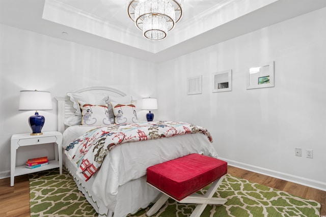 bedroom featuring a chandelier, a tray ceiling, ornamental molding, and wood finished floors