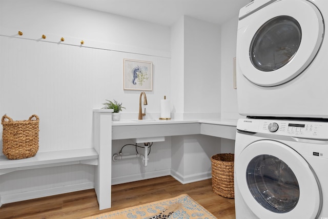 washroom with laundry area, baseboards, stacked washer and clothes dryer, wood finished floors, and a sink