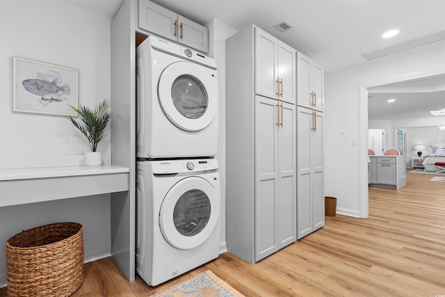 laundry room with light wood finished floors, visible vents, and stacked washer / drying machine