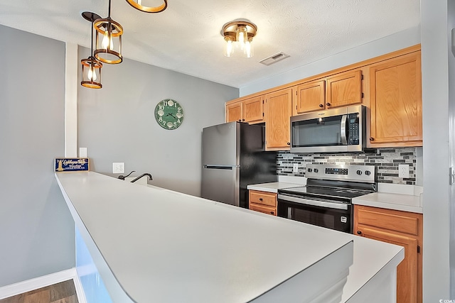 kitchen with appliances with stainless steel finishes, pendant lighting, kitchen peninsula, and decorative backsplash