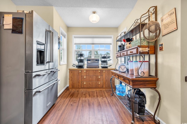 kitchen with stainless steel fridge, baseboards, dark wood-style floors, brown cabinets, and a textured ceiling