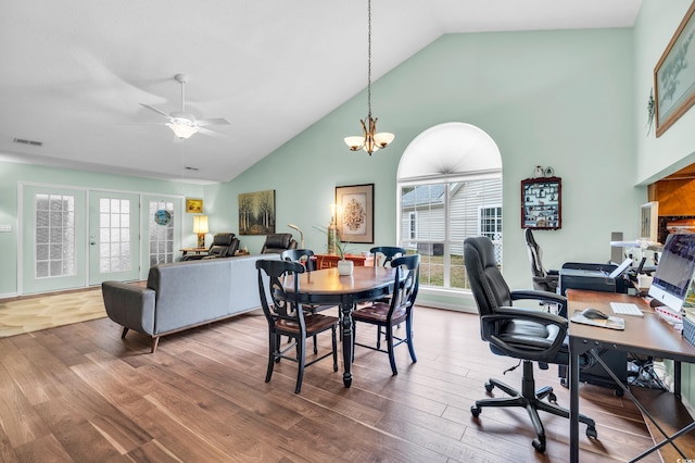 dining space featuring high vaulted ceiling, ceiling fan with notable chandelier, visible vents, and wood finished floors