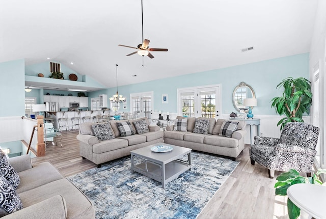 living room featuring a wainscoted wall, visible vents, wood finished floors, high vaulted ceiling, and ceiling fan with notable chandelier