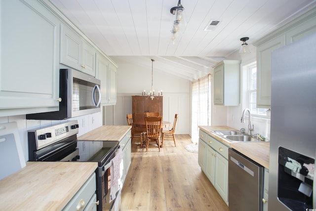 kitchen featuring butcher block countertops, sink, stainless steel appliances, decorative light fixtures, and vaulted ceiling