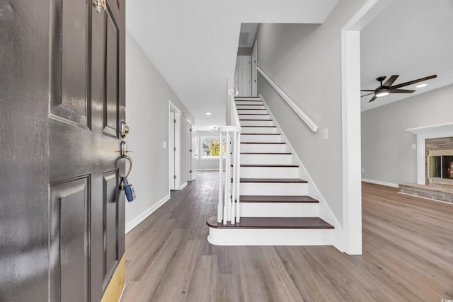 foyer entrance featuring a warm lit fireplace, stairway, wood finished floors, and baseboards