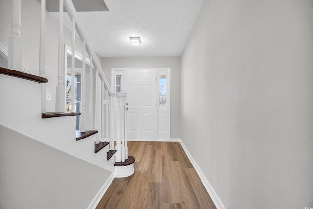 foyer featuring a textured ceiling, wood finished floors, stairs, and baseboards