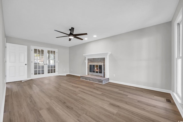 unfurnished living room featuring wood finished floors, visible vents, baseboards, french doors, and a glass covered fireplace