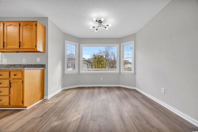 unfurnished dining area with a healthy amount of sunlight, a notable chandelier, baseboards, and wood finished floors