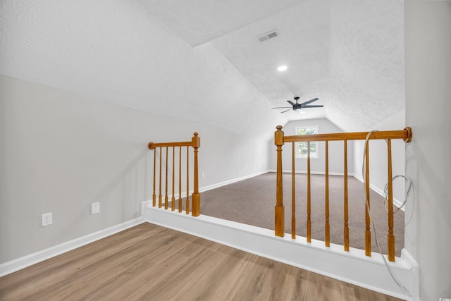 bonus room featuring a textured ceiling, wood finished floors, visible vents, baseboards, and vaulted ceiling