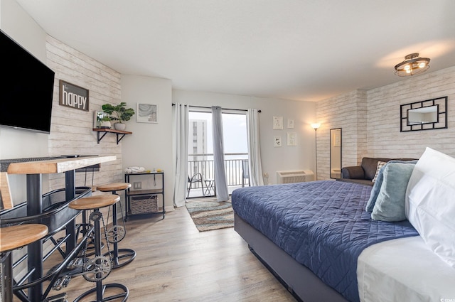 bedroom with access to exterior, light hardwood / wood-style flooring, and brick wall