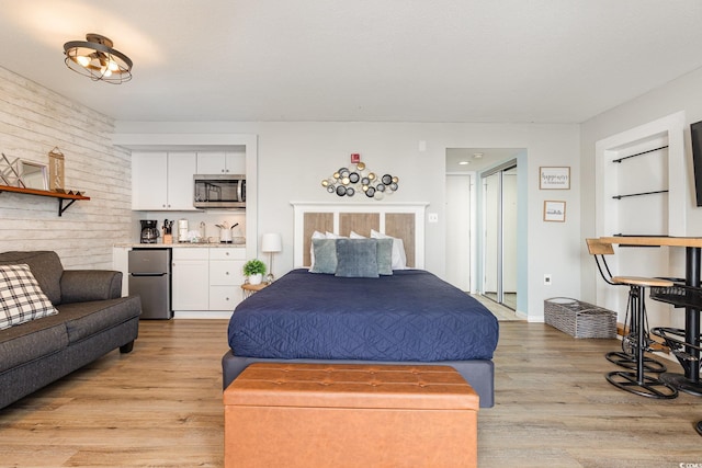 bedroom with light wood-type flooring, bar, and stainless steel refrigerator