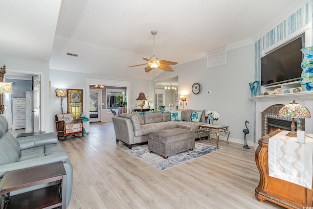 living room with a tile fireplace, vaulted ceiling, ceiling fan, and light hardwood / wood-style floors