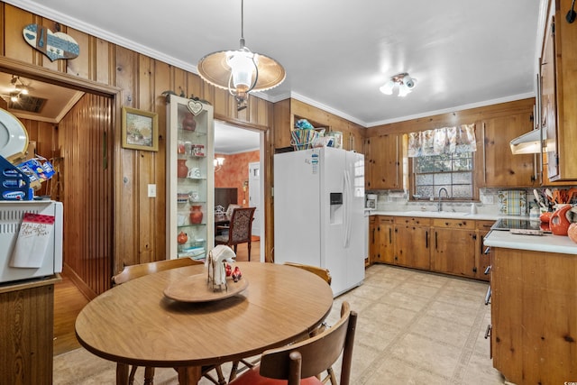 kitchen with sink, wood walls, crown molding, decorative light fixtures, and white fridge with ice dispenser