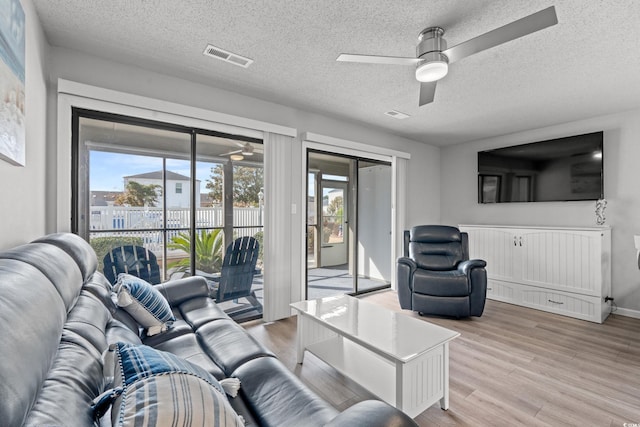 living room featuring ceiling fan, a textured ceiling, and light hardwood / wood-style floors