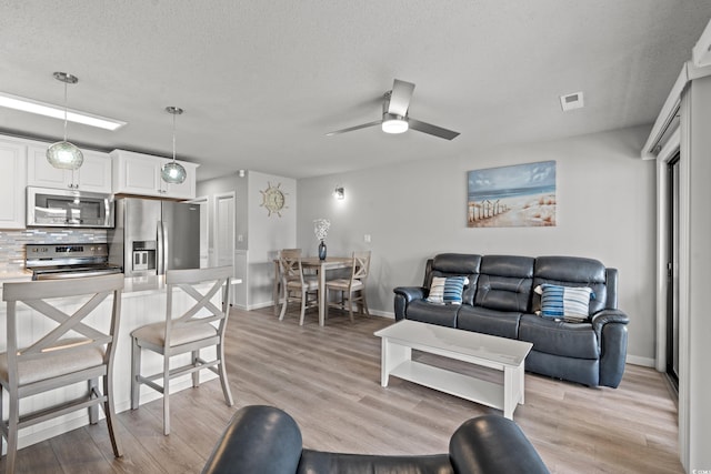 living room with ceiling fan, light hardwood / wood-style flooring, and a textured ceiling