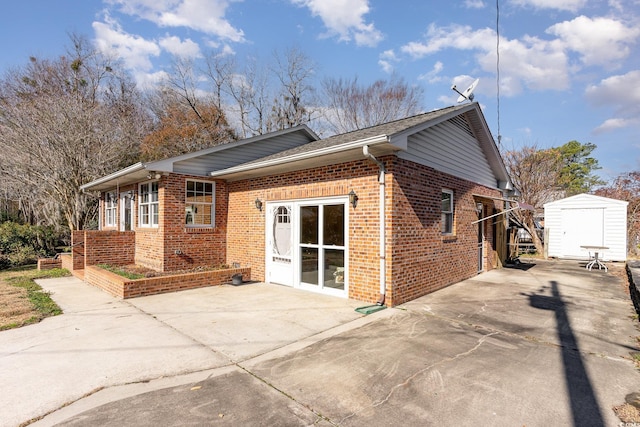 view of side of property featuring a storage shed, concrete driveway, brick siding, and an outdoor structure