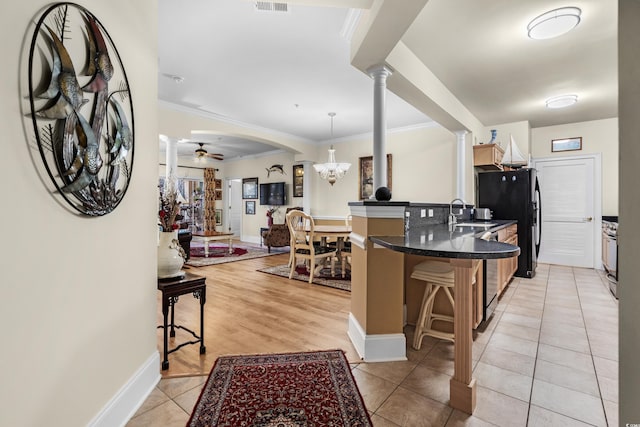 kitchen featuring black refrigerator, ceiling fan with notable chandelier, pendant lighting, decorative columns, and a kitchen breakfast bar