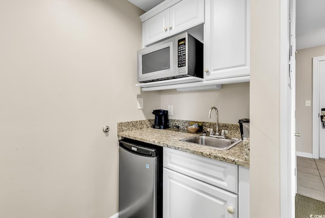 kitchen featuring sink, white cabinets, tile patterned flooring, fridge, and light stone countertops