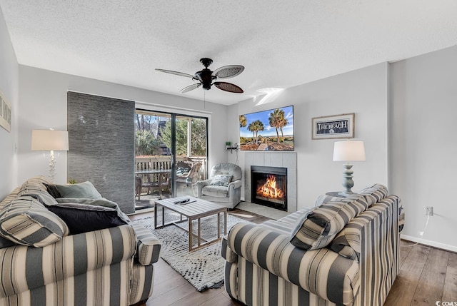 living room featuring hardwood / wood-style flooring, ceiling fan, a textured ceiling, and a fireplace