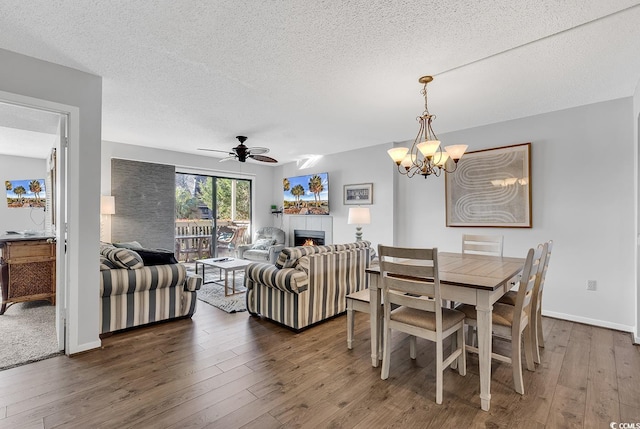 dining room with ceiling fan with notable chandelier, dark wood-type flooring, and a textured ceiling