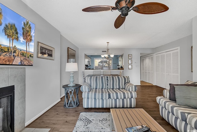 living room with a tiled fireplace, hardwood / wood-style flooring, ceiling fan with notable chandelier, and a textured ceiling