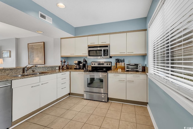 kitchen with appliances with stainless steel finishes, sink, white cabinets, light tile patterned floors, and light stone countertops