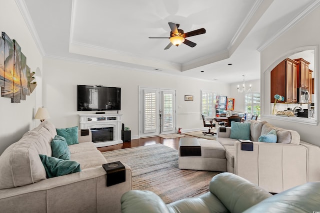 living room featuring hardwood / wood-style flooring, ornamental molding, a tray ceiling, and ceiling fan with notable chandelier