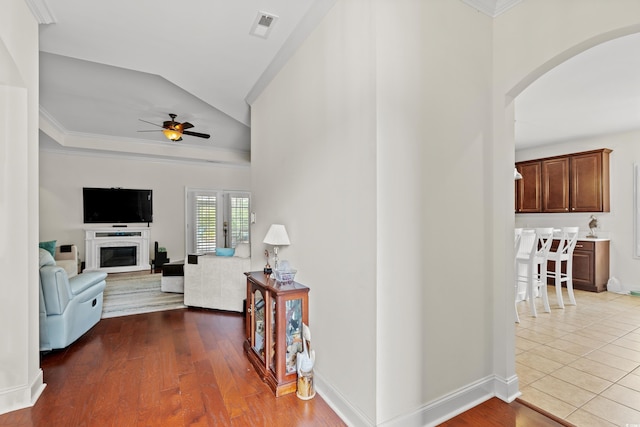 corridor with hardwood / wood-style floors, vaulted ceiling, and ornamental molding