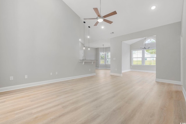 unfurnished living room with ceiling fan with notable chandelier, vaulted ceiling, and light wood-type flooring