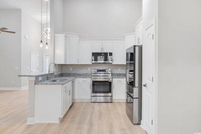 kitchen with sink, appliances with stainless steel finishes, white cabinetry, a high ceiling, and light stone countertops