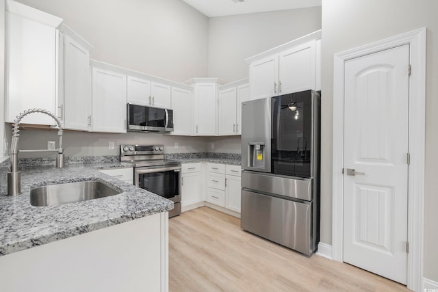 kitchen with stainless steel appliances, white cabinetry, light stone countertops, and sink