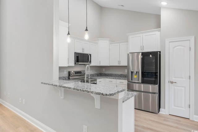 kitchen with appliances with stainless steel finishes, pendant lighting, white cabinetry, a breakfast bar area, and kitchen peninsula