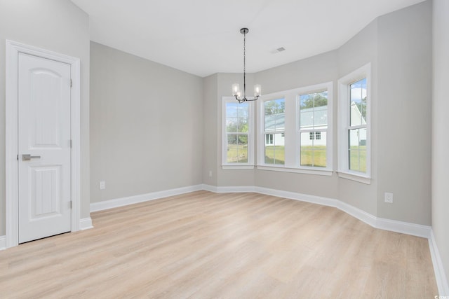 spare room featuring a notable chandelier and light wood-type flooring