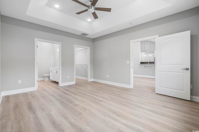 unfurnished bedroom featuring a closet, a spacious closet, light hardwood / wood-style flooring, and a tray ceiling