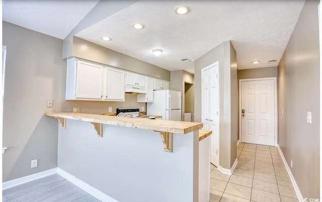 kitchen featuring a peninsula, white appliances, a breakfast bar, and light countertops