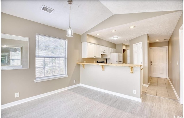 kitchen with a peninsula, visible vents, baseboards, vaulted ceiling, and freestanding refrigerator